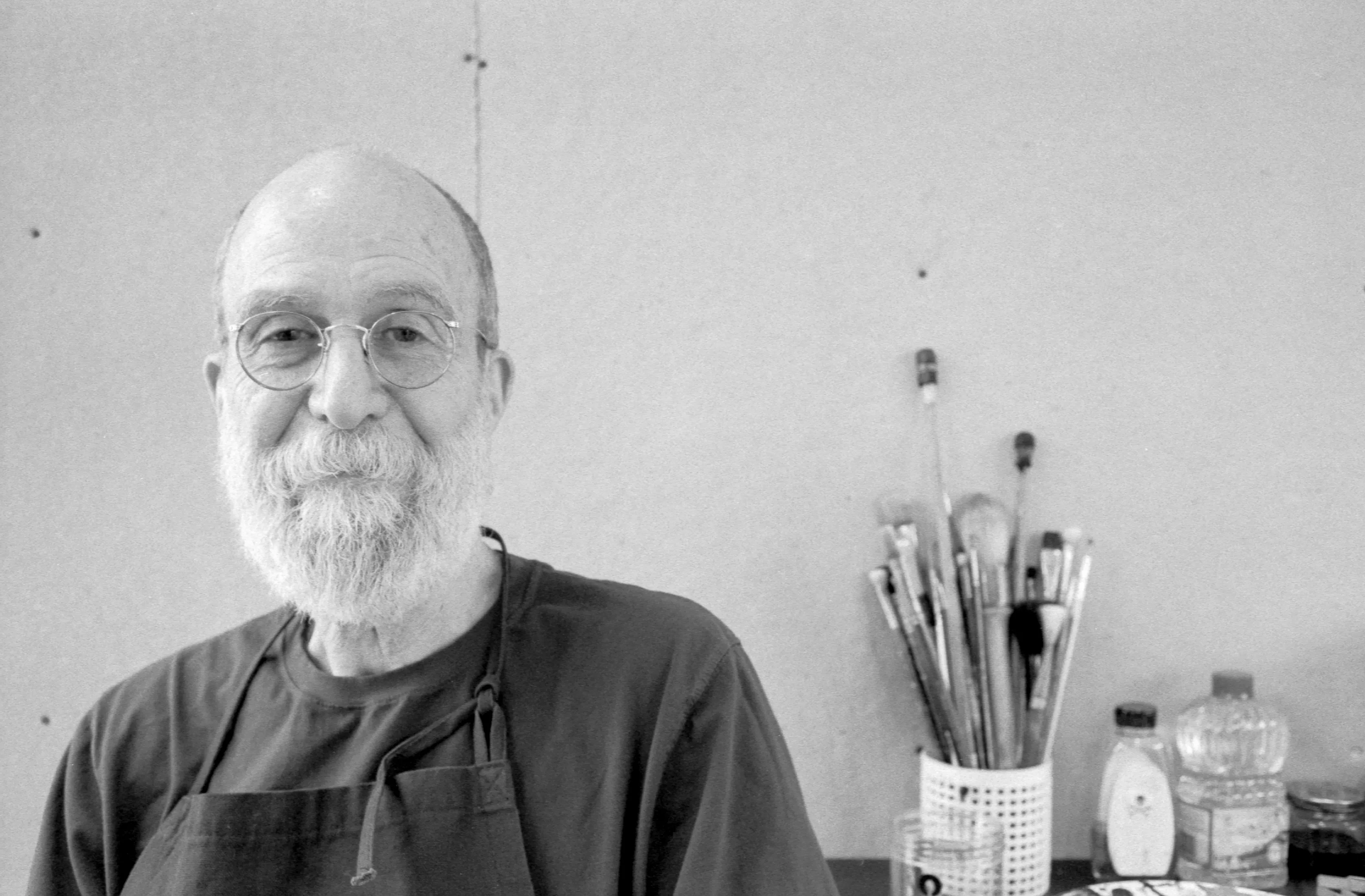 Kind old man wearing glasses with art supplies behind him
